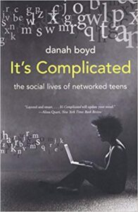 A person seated on the floor uses a laptop amid scattered letters. Book cover: "It's Complicated: The Social Lives of Networked Teens."