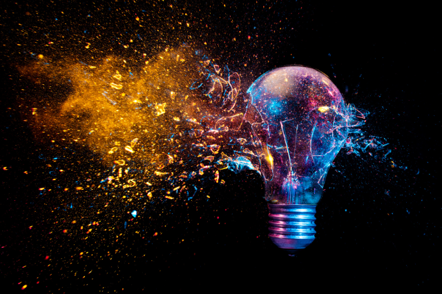 A colorful explosion of light and particles around a shattering light bulb against a dark background, creating a dynamic and vibrant visual effect.